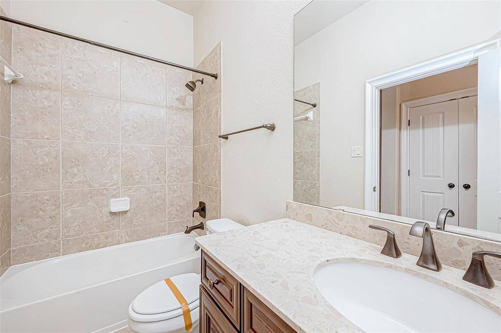 This bathroom features a modern design with a tiled shower-tub combo, a sleek countertop with an under-mount sink, and bronze fixtures. Neutral tones create a clean, inviting atmosphere.