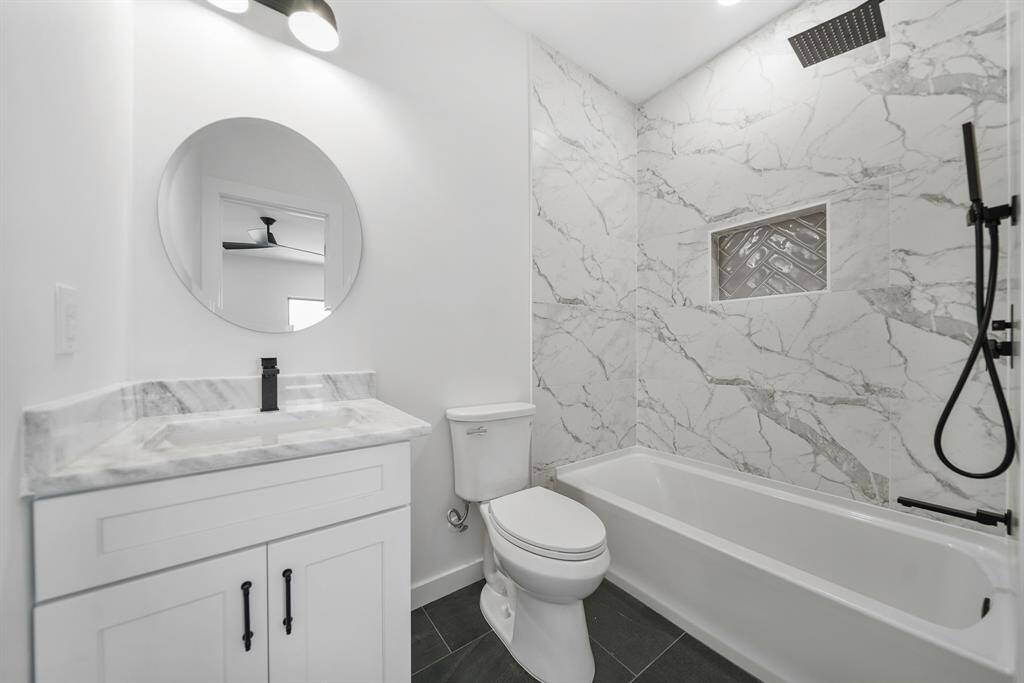 Attached bathroom features a sleek design with a round mirror above a vanity with a marble countertop, and contemporary fixtures.