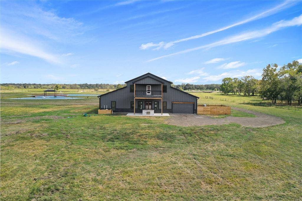 A modern barn-style home set on 15 sprawling acres. The property features a pond with a bridge and gazebo, surrounded by greenery and trees, offering a serene and private rural setting.