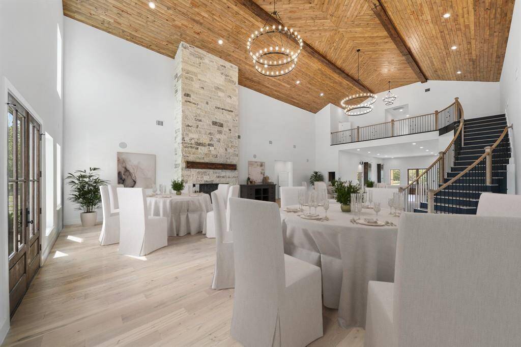 This photo showcases the spacious elegant room with a high vaulted wooden ceiling and large stone fireplace. The open layout has endless possibilities, including an ideal setting for a venue. Virtual staged setting