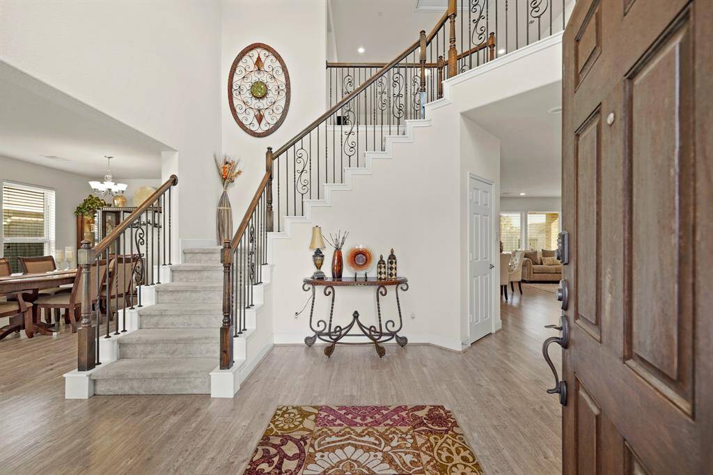 The grand entryway has an elegant wrought-iron staircase, warm wood flooring, and an open layout that flows into the dining and living areas.