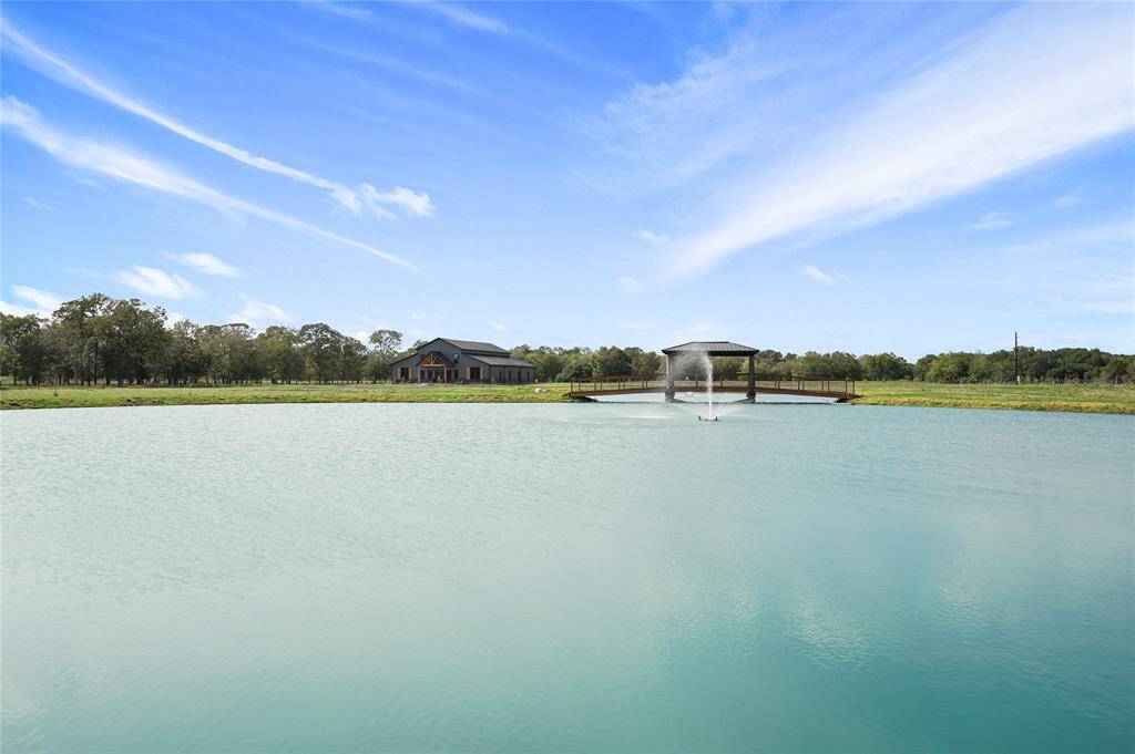 This property features a spacious home set against a scenic backdrop with a large pond and fountains, surrounded by lush greenery, offering a tranquil and picturesque setting.