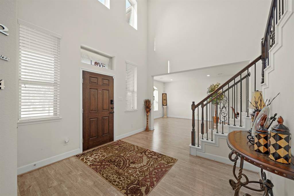 The bright and inviting foyer with soaring ceilings, abundant natural light, and elegant details like a wrought-iron staircase and wood accents
