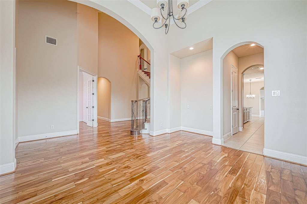 Spacious, open-concept living area with high ceilings and elegant hardwood floors. Arched doorways and a stylish chandelier add sophistication, while the space flows seamlessly to a staircase and additional rooms.