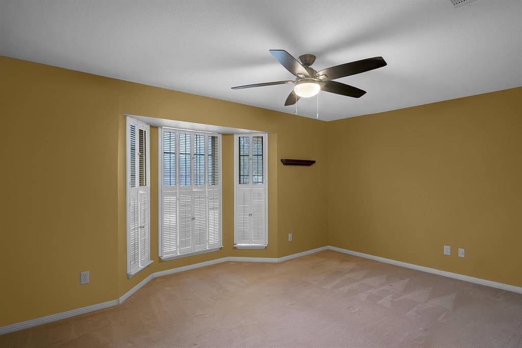 Bedroom #2 upstairs is spacious and inviting, featuring plush neutral carpet and a walk-in closet for ample storage. A ceiling fan with light fixture ensures comfort, while large windows flood the room with natural light, creating a bright and airy atmosphere.