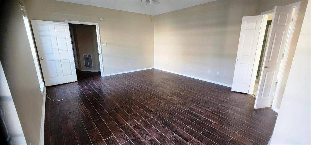 This room features rich, dark wood-look flooring and neutral-colored walls, offering a spacious and modern feel. It includes multiple doors leading to adjoining rooms, enhancing accessibility and flow.