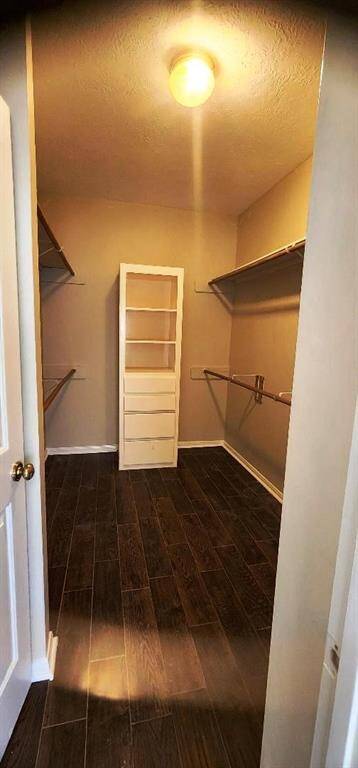 This is a spacious walk-in closet featuring dark wood flooring, multiple hanging rods, and a central shelving unit for ample storage. The overhead lighting provides good illumination.