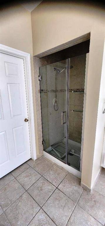 This photo shows a bathroom with a glass-enclosed shower featuring tiled walls and a built-in showerhead. The floor is tiled, and there's a white door nearby, likely leading to another room or storage.