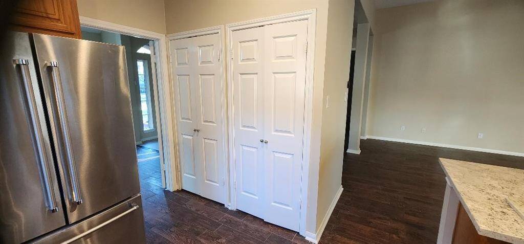 This photo showcases a modern kitchen area with stainless steel appliances, including a double-door refrigerator. It features hardwood flooring, neutral walls, and ample natural light from adjacent windows. There are multiple white-paneled doors leading to storage or additional rooms, enhancing functionality. The kitchen counter has a light, speckled surface, adding to the contemporary feel.
