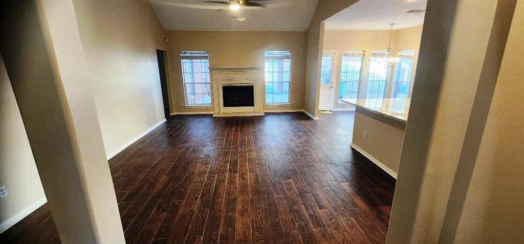 This photo showcases a spacious living area with dark hardwood flooring, a central fireplace, and large windows providing ample natural light. The room opens to a dining area with a modern light fixture and access to a fenced outdoor space.