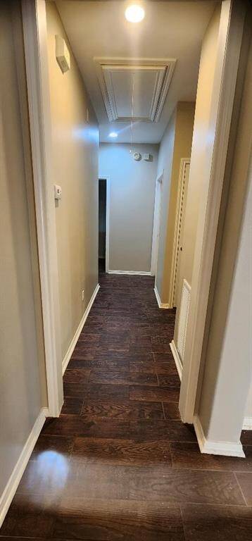 This photo shows a narrow hallway with dark hardwood flooring and neutral-colored walls. It features recessed ceiling lighting and a closed door at the end, along with a few wall-mounted fixtures.