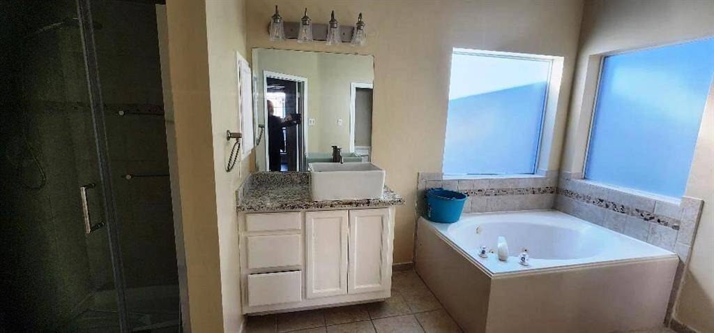 This bathroom features a spacious soaking tub with adjacent frosted windows for privacy, a modern glass-enclosed shower, and a stylish vanity with a granite countertop and large mirror, providing a bright and inviting space.