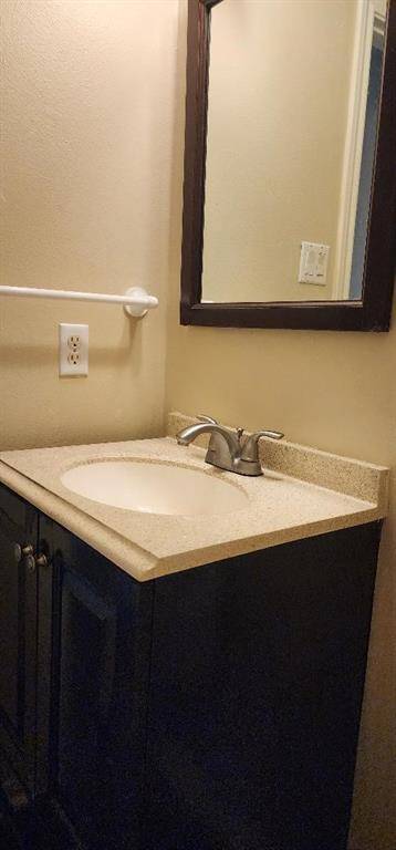This photo shows a compact bathroom vanity with a beige countertop and an undermount sink. It features a dark wood cabinet and a matching framed mirror above. The walls are painted in a neutral tone, and there's a towel holder on the side.