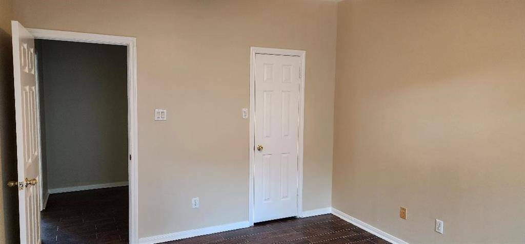 This room features neutral beige walls, a white door, and dark flooring, creating a simple and clean space. It's versatile for various uses, like a bedroom or office.