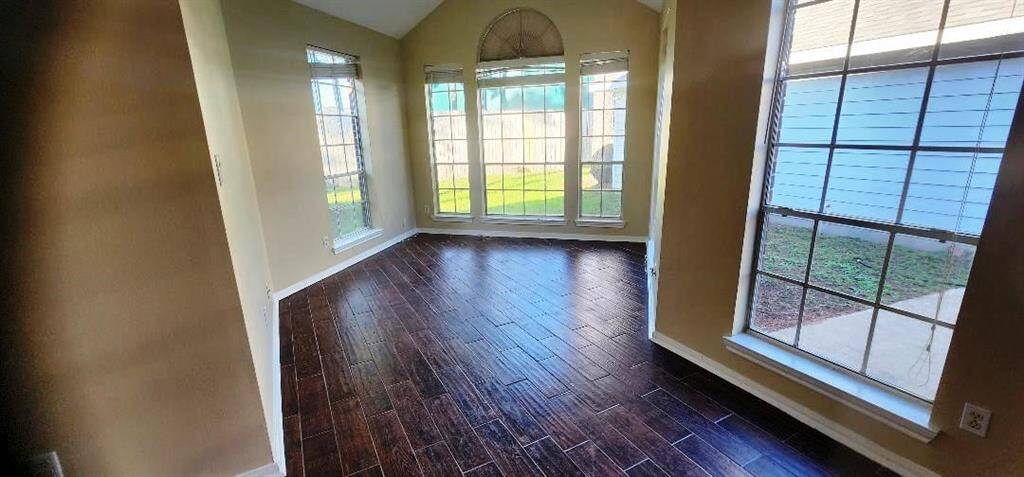 This room features rich wood-look flooring and ample natural light from large windows, offering a bright and inviting space with views of the backyard.