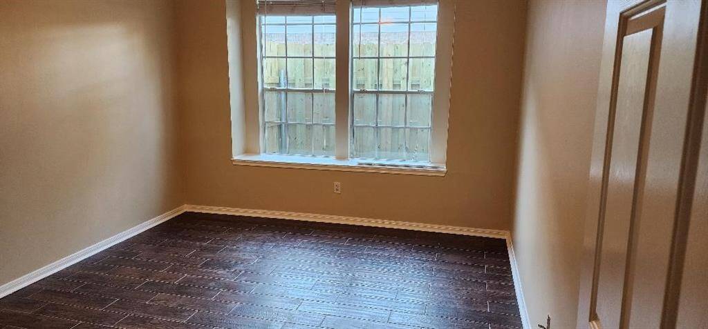 This room features warm beige walls and dark wood flooring, highlighted by a large window that provides natural light. Ideal for a cozy bedroom or home office.