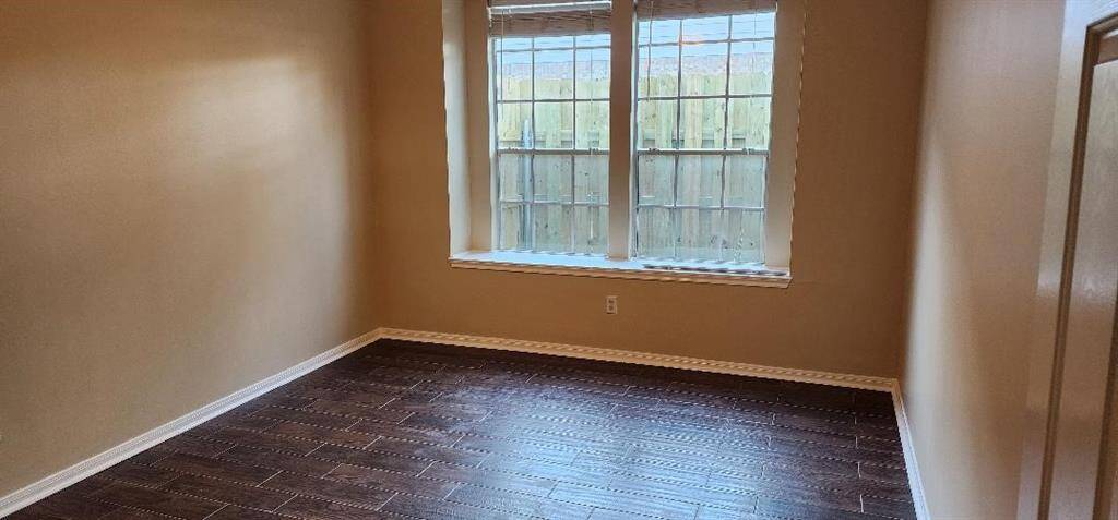 This room features warm beige walls and rich dark wood flooring, illuminated by natural light from a large window with a view of the fenced backyard.