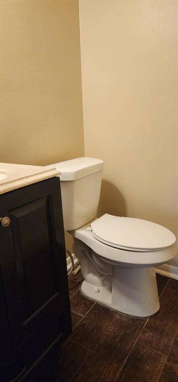 This bathroom features a modern design with a white toilet and a dark wood vanity, complemented by neutral wall paint and wood-look tile flooring.