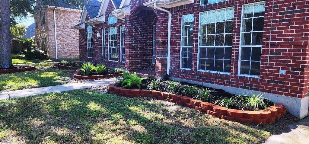 This photo showcases a charming brick exterior of a home with large windows. The front yard features well-maintained landscaping, including flower beds with brick edging and lush green plants, creating an inviting curb appeal.