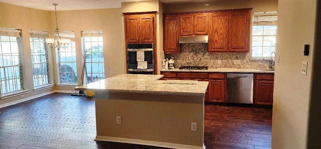 This photo showcases a spacious kitchen with rich wooden cabinets, granite countertops, and stainless steel appliances. The open layout flows into a bright dining area with large windows and hardwood floors, enhancing natural light.