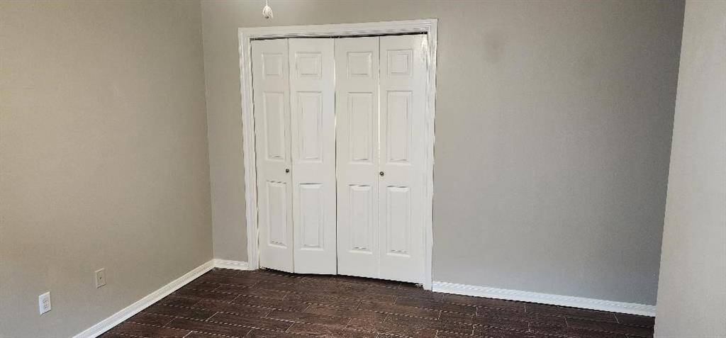 This room features neutral-colored walls and dark wood flooring, with a set of white double doors for closet space, creating a clean and versatile space.