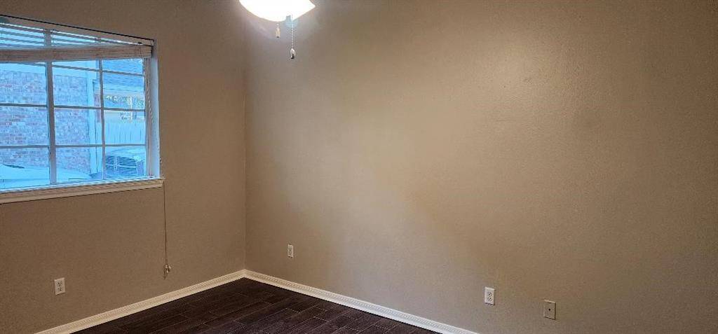 This is a small, neutral-toned room with dark wood flooring and a window providing natural light. It features a ceiling fan and has a simple, clean design, ideal for an office or guest room.
