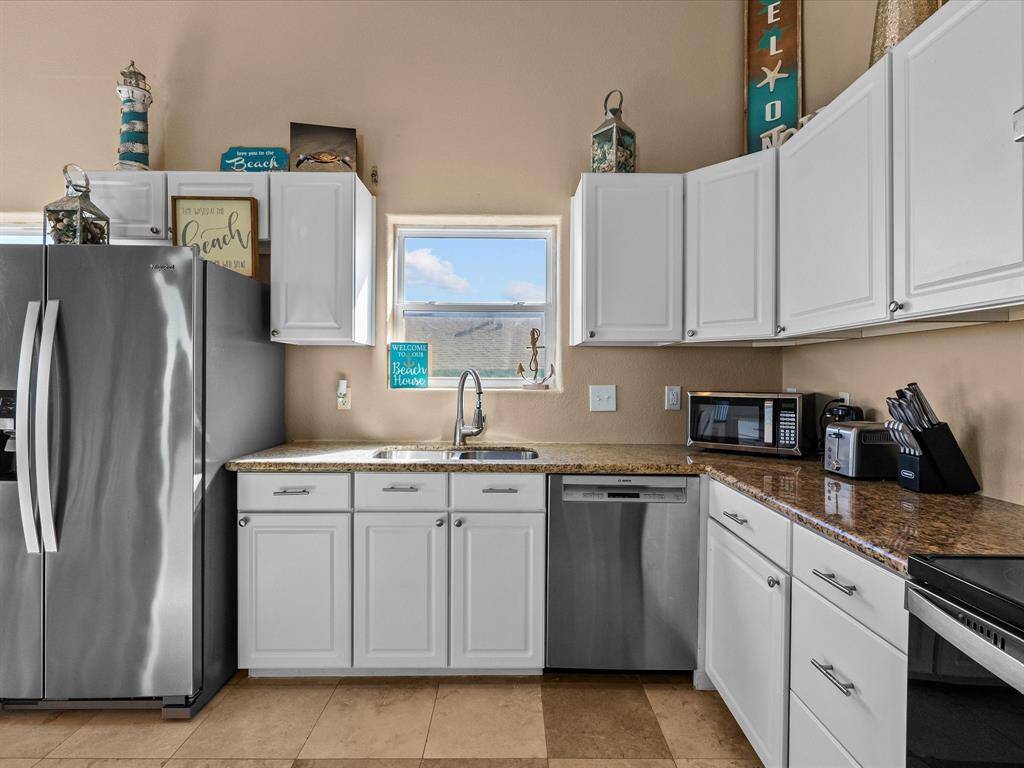 Modern kitchen with sleek stainless steel appliances, white cabinetry, and granite countertops. The space is brightened by natural light from a small window, offering a cozy and functional cooking area. Decor elements add a charming touch.