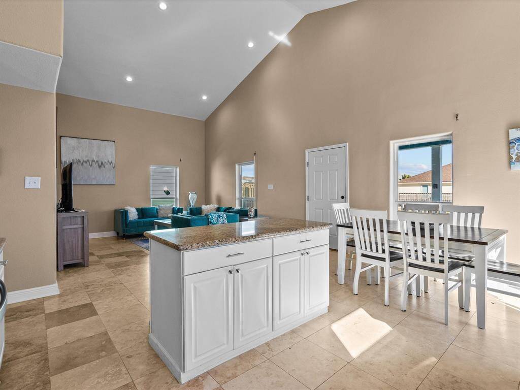 This spacious living area features high ceilings, a neutral color palette, and ample natural light. It includes a modern kitchen island, a dining area with a large window, and a cozy seating area with contemporary furniture.