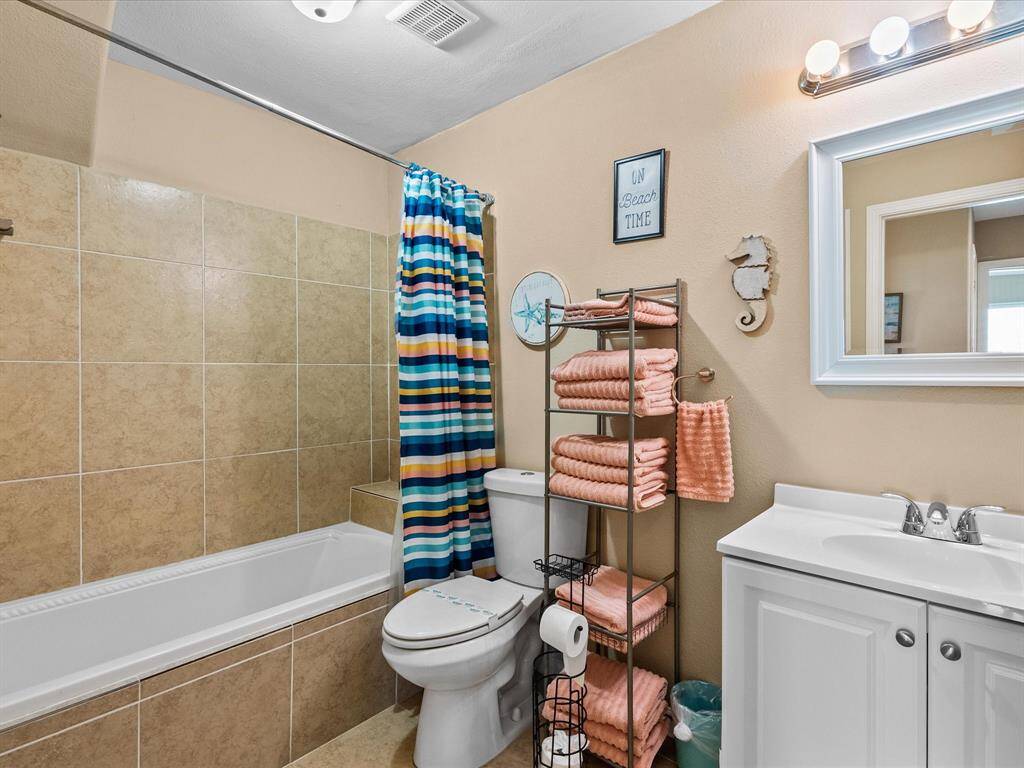 This bathroom features a tiled bathtub with a colorful striped shower curtain, a modern vanity with a mirror, and ample storage with a towel rack and shelving, creating a bright and functional space.