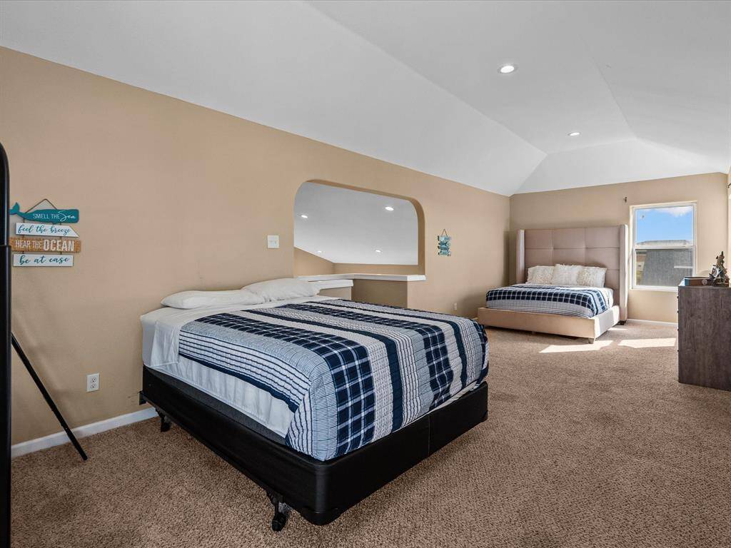 Spacious bedroom with two beds, neutral tones, and cozy carpeting. Includes recessed lighting and a bright window, creating a welcoming atmosphere.