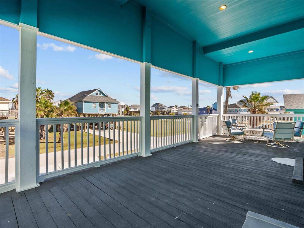This spacious outdoor deck features a covered area with teal accents, offering ample space for seating and entertainment. The view includes neighboring houses and palm trees, creating a relaxed, coastal atmosphere.