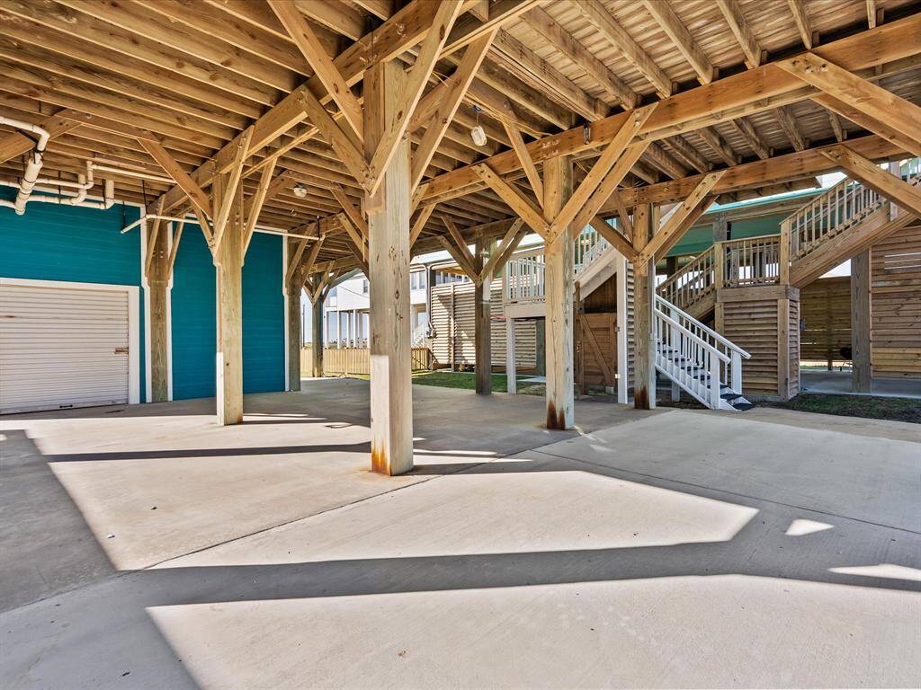 This photo features an elevated coastal-style home with a spacious covered area beneath, supported by sturdy wooden beams. It includes a garage door and outdoor staircase, perfect for weather protection and additional storage or parking space.