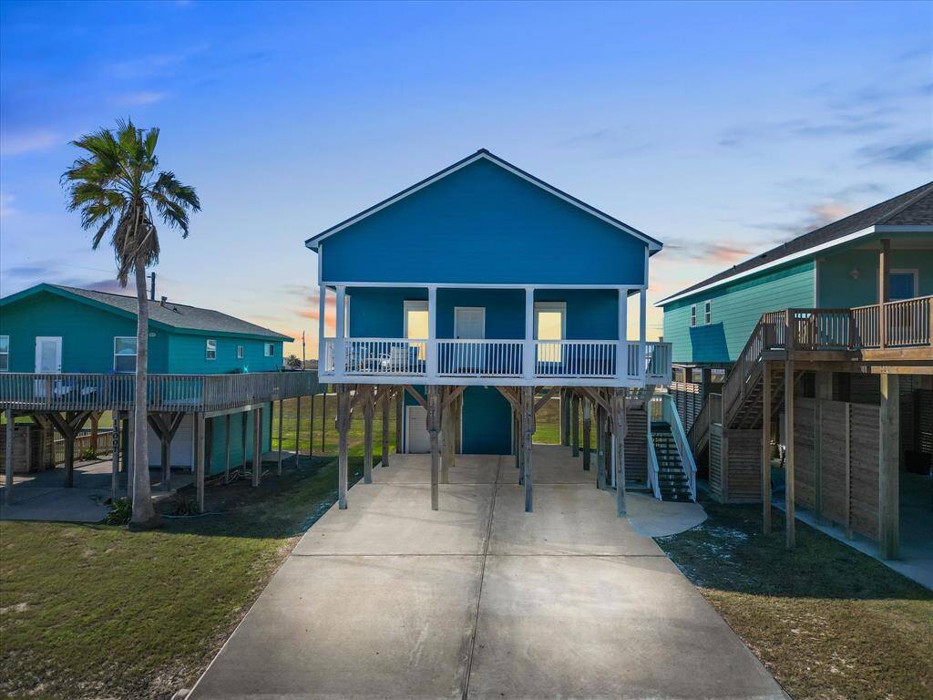 This open-concept living area features high ceilings, abundant natural light, and stylish decor. The space includes a modern kitchen with white cabinetry and stainless steel appliances, a cozy dining area, and a comfortable living room with vibrant blue seating, creating an inviting atmosphere.