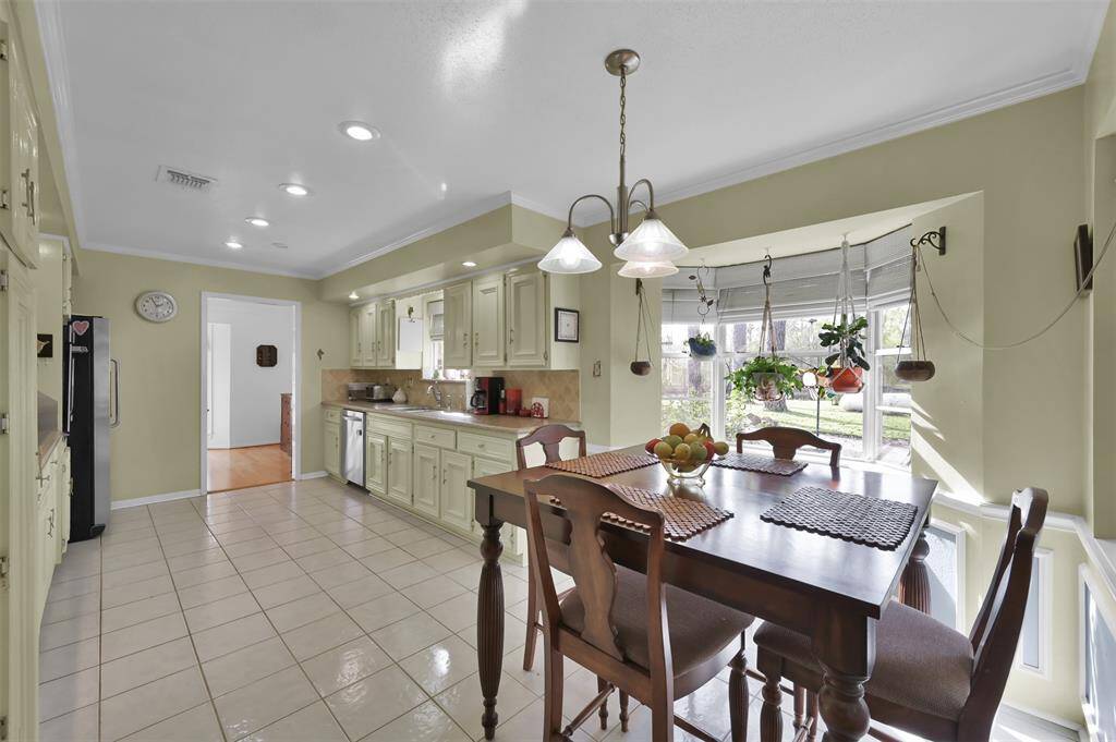 This bright kitchen features ample cabinetry, recessed lighting, and a cozy breakfast nook by a bay window with hanging plants
