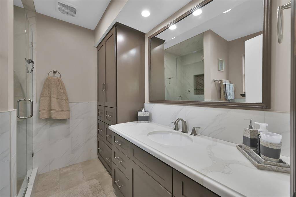 Renovated bathroom features a modern design with a large mirror, sleek vanity with ample storage, and a glass-enclosed shower. Neutral tones and recessed lighting create a bright, inviting space.