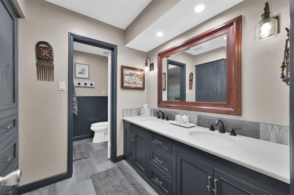 This bathroom features a modern, double-sink vanity with dark cabinetry and a large framed mirror and custom built in cabinetry for additional storage