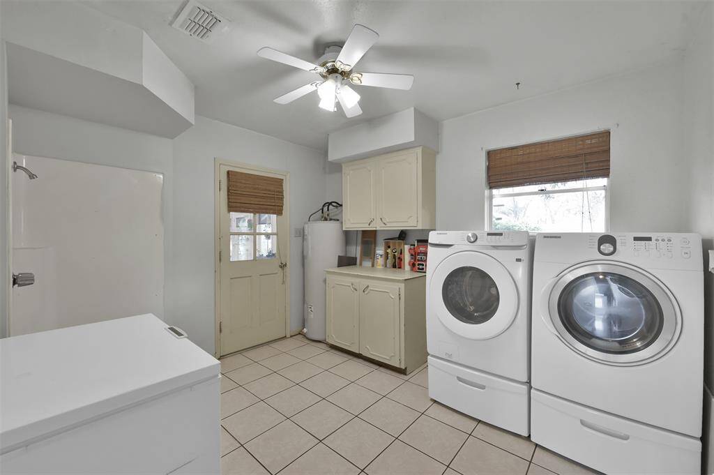 Spacious laundry room with tile flooring, featuring a washer and dryer, storage cabinets, and a door leading to the sunroom.