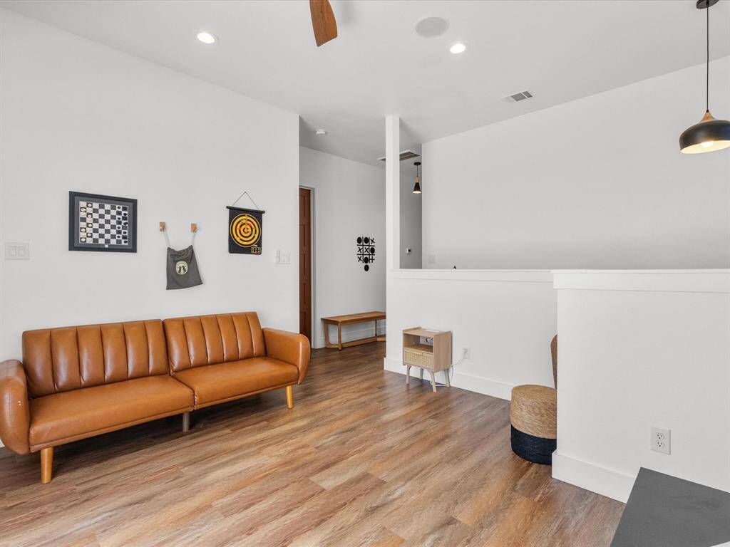 This photo showcases a bright, modern living area with wood flooring, white walls, and recessed lighting. It features a stylish brown sofa, contemporary wall art, and a pendant light, creating a cozy, inviting atmosphere.
