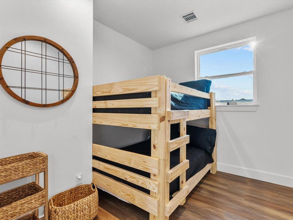 This room features a cozy wooden bunk bed with a window offering natural light. The space includes a stylish round mirror and woven storage baskets, creating a functional and inviting atmosphere.