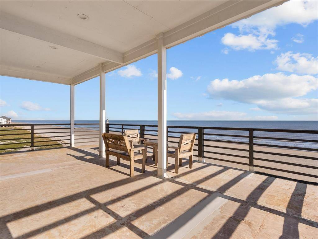 This photo showcases a spacious, covered outdoor terrace with stunning ocean views. It features seating for relaxation, framed by clear blue skies and gentle waves, ideal for enjoying coastal living.