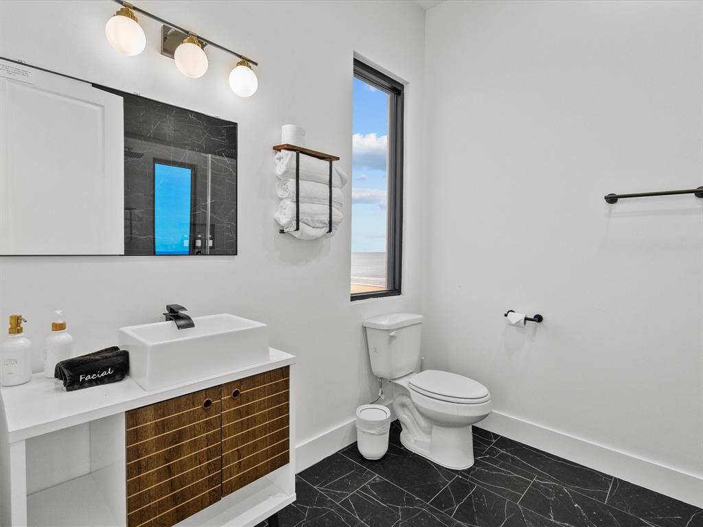 Modern bathroom with sleek black marble flooring, a white vanity with under-sink storage, and a large mirror. It features a contemporary vessel sink, black fixtures, and a window offering natural light and a view.