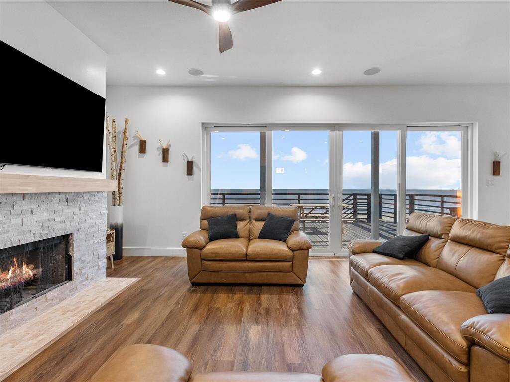 This inviting living room features a cozy fireplace, sleek wood flooring, and comfortable leather seating. Large windows offer stunning ocean views and plenty of natural light, creating a perfect blend of comfort and elegance.