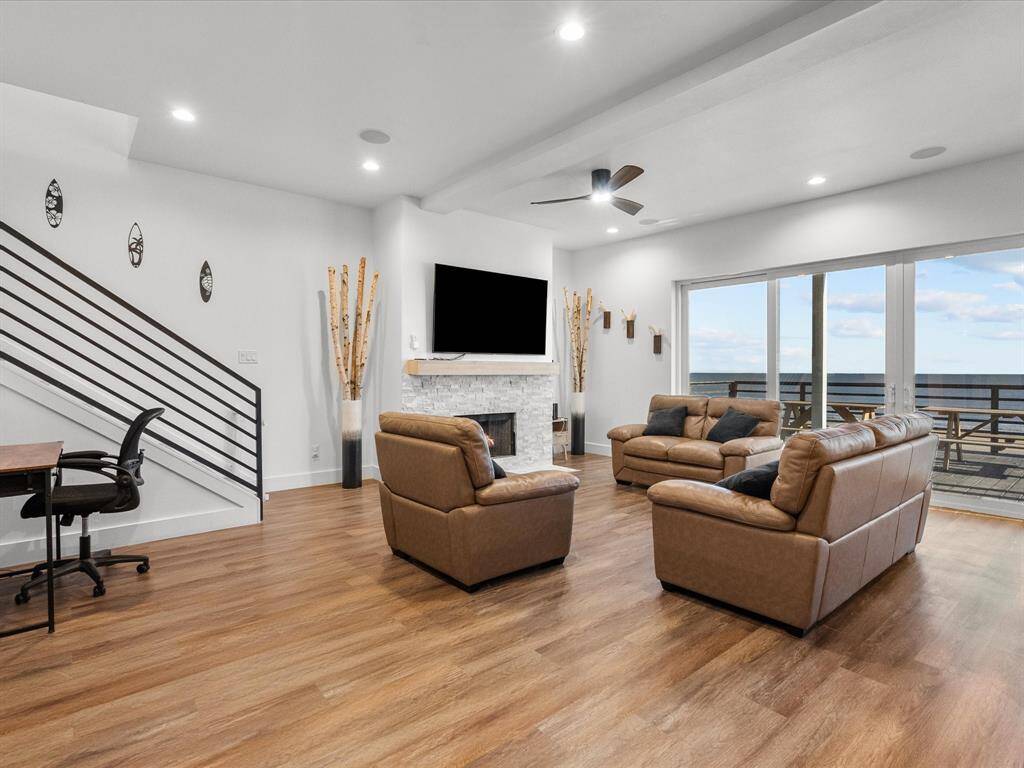 Spacious living room with modern design, featuring hardwood floors, leather seating, and a sleek fireplace. Large windows offer stunning ocean views, complemented by a balcony for outdoor enjoyment. Perfect for relaxing and entertaining.