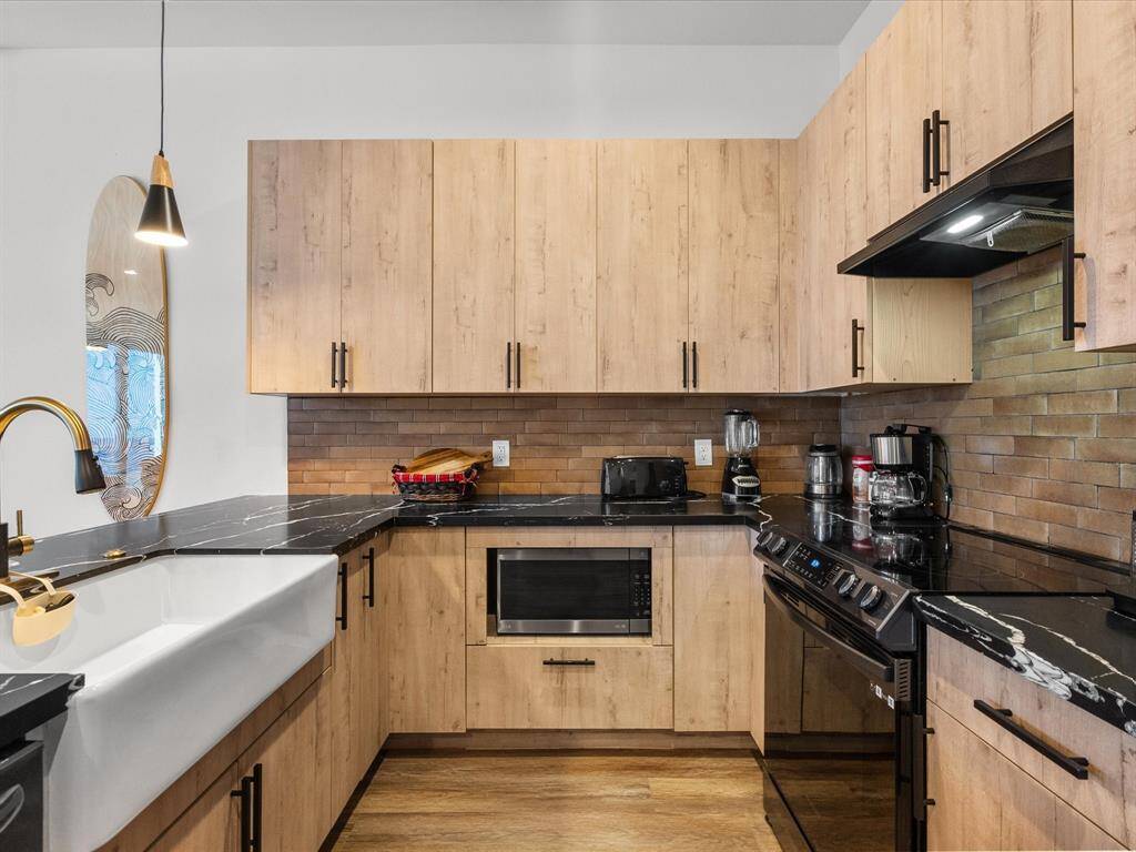 Modern kitchen with sleek wood cabinetry, dark marble countertops, and stainless steel appliances. Features a farmhouse sink, brick-style backsplash, and stylish pendant lighting.