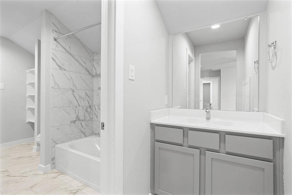 This secondary jack-n-jill bath features tile flooring, bath/shower combo with tile surround, stained wood cabinets, beautiful light countertops, mirror, sleek fixtures and modern finishes.