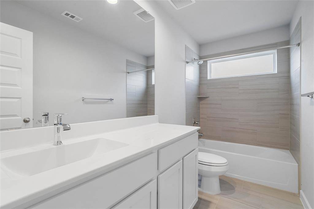 Secondary bedroom features plush carpet, custom paint, high ceilings with ceiling fan, and a large window with privacy blinds. This secondary bedroom shares a jack-n-jill bathroom and access to its private vanity sink.
