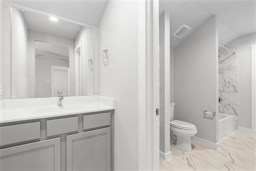 This secondary jack-n-jill bath features tile flooring, bath/shower combo with tile surround, stained wood cabinets, beautiful light countertops, mirror, sleek fixtures and modern finishes.