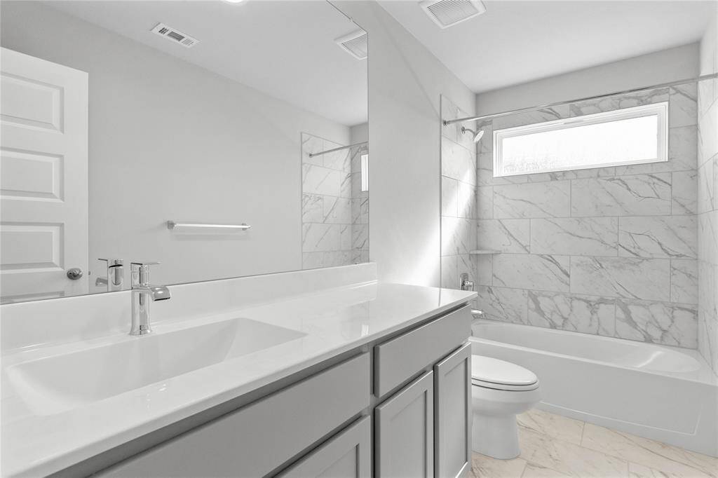 Secondary bath features tile flooring, bath/shower combo with tile surround, stained wood cabinets, beautiful light countertops, mirror, sleek fixtures and modern finishes.