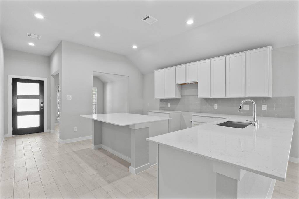 This stunning kitchen displays stained cabinets, custom neutral paint, quartz countertops, light modern backsplash, oversized kitchen island with extra storage, breakfast bar, recessed lighting, high ceilings and pantry.