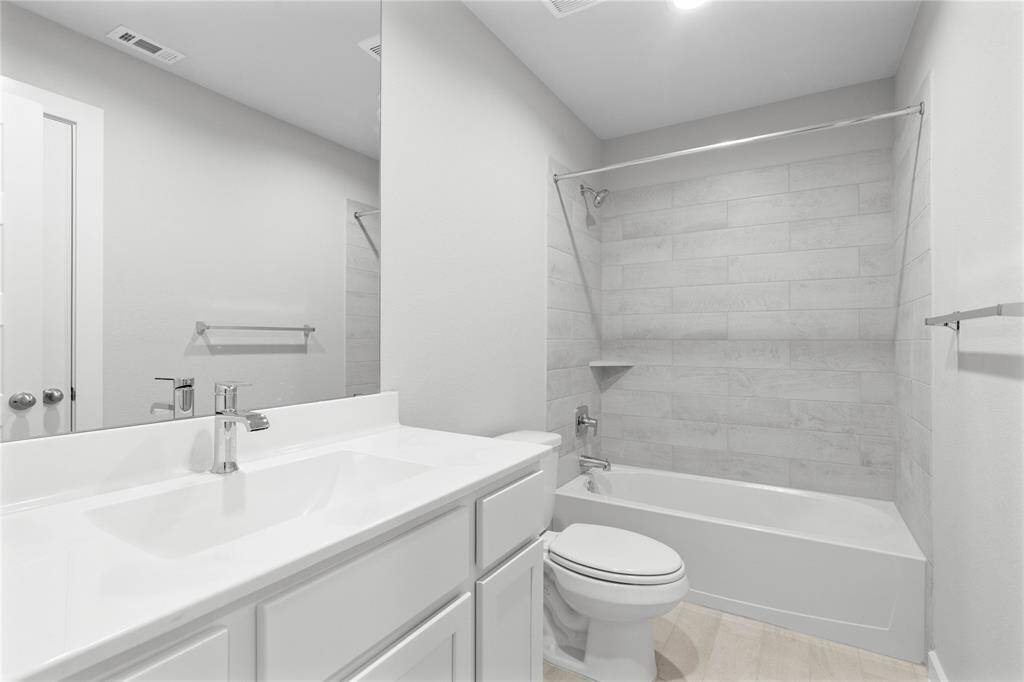 Secondary bath features tile flooring, bath/shower combo with tile surround, stained cabinets, beautiful light countertops, mirror, sleek fixtures and modern finishes.